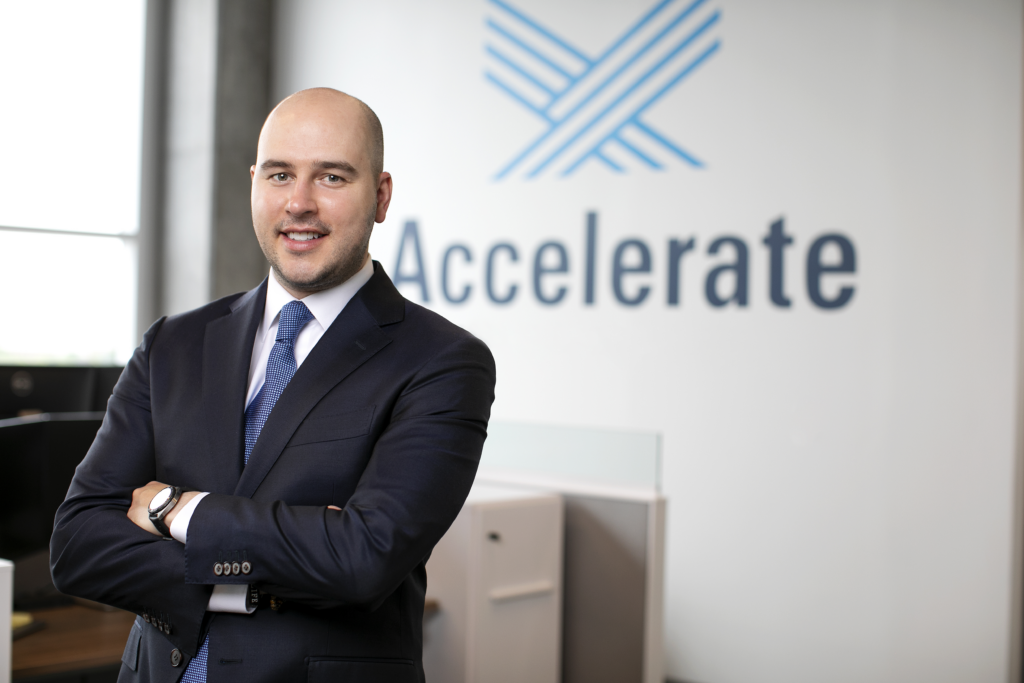 Accelerate's Brennan Potts standing in front of the Accelerate logo plastered on a wall