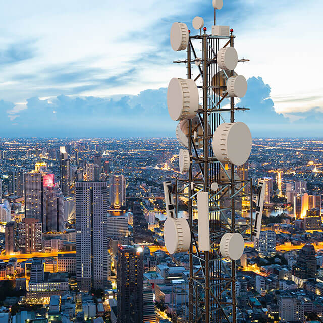 Close up view of the top of a communications tower on top of a skyscraper with a large, sprawling city below