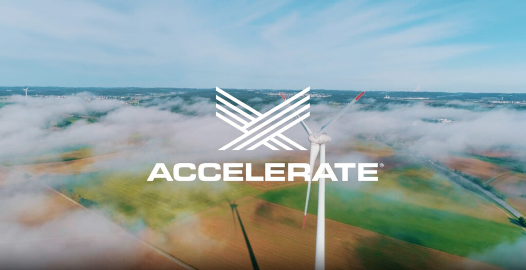 The Accelerate logo superimposed over a wind turbine rising above clouds in a country side